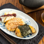 A rectangular plate containing three flavors of mochi (sweet red bean, sweet soybean flour, and soy sauce and nori seaweed).